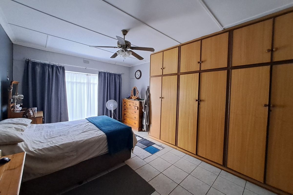 A bedroom featuring tiled flooring, a ceiling fan, and extensive built-in wooden cupboards providing ample storage space.