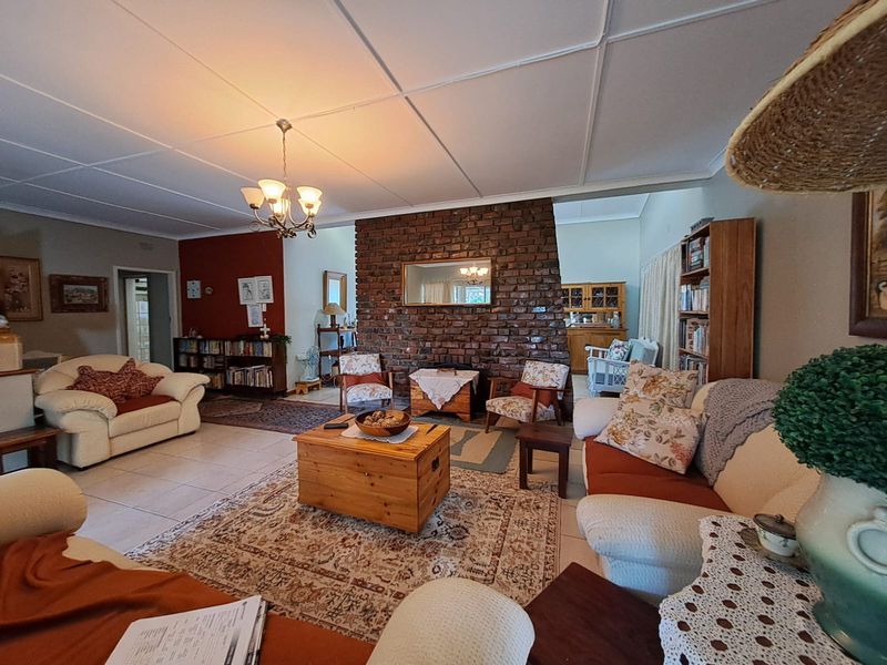 Spacious living room featuring an exposed brick fireplace, tiled flooring, and classic ceiling tiles, offering a warm and traditional atmosphere.