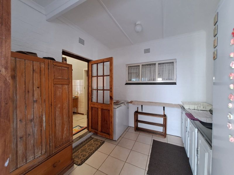 A functional scullery area featuring tiled flooring, built-in cabinetry, and a timber-framed door leading to an adjacent room.