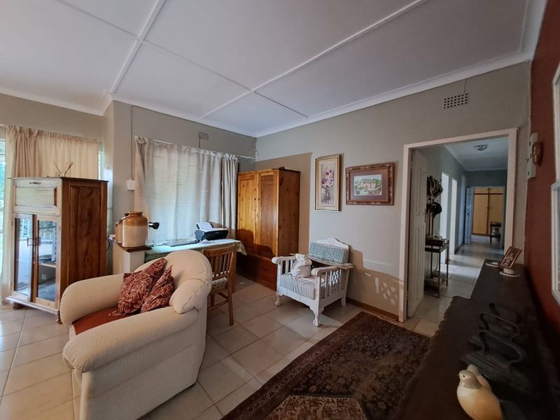 A living area featuring tiled flooring and ceiling detailing, with an adjacent hallway leading to other parts of the home.