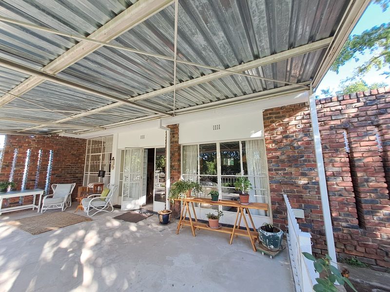 A covered outdoor patio featuring exposed brick walls, concrete flooring, and a corrugated metal roof, providing a functional space for outdoor living.