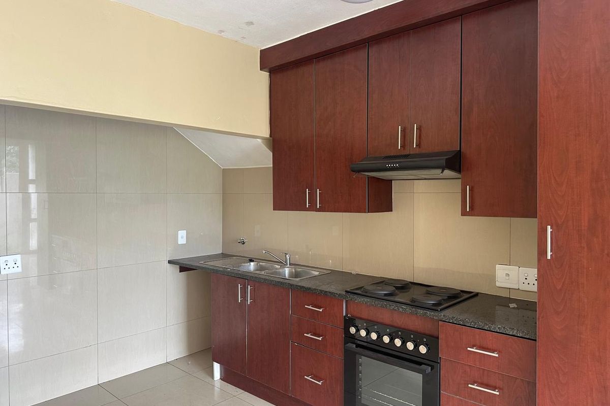 A functional kitchen featuring dark wood cabinetry, granite countertops, a built-in oven with hob, and an extractor fan, complemented by neutral tiled walls and flooring.