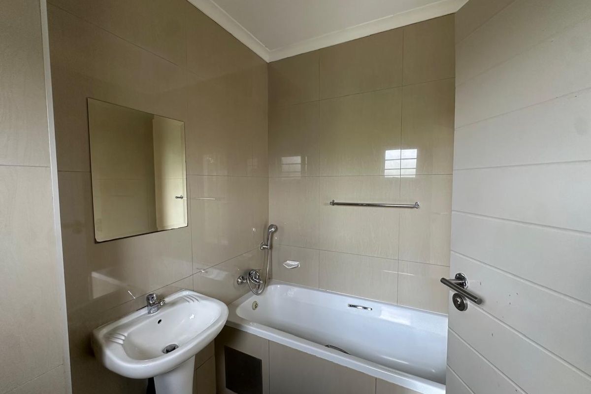A functional bathroom featuring a pedestal basin, a bathtub with a handheld shower attachment, and neutral wall tiling.