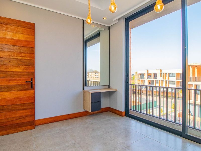 A bright, modern bedroom featuring tiled floors, a built-in vanity, and a large sliding glass door leading to a balcony with neighborhood views.