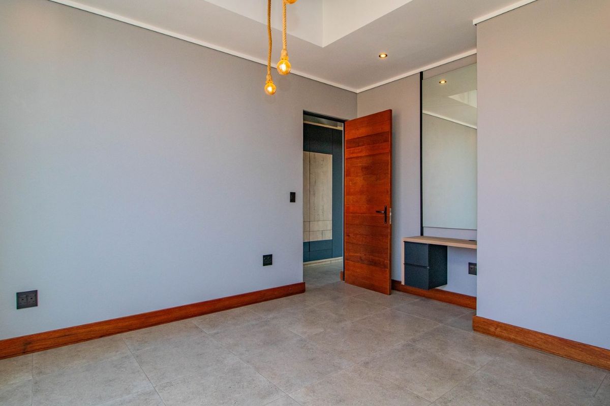 A clean, modern bedroom featuring tiled floors, a built-in vanity with mirror, and a warm wooden door, offering a neutral canvas for personalization.