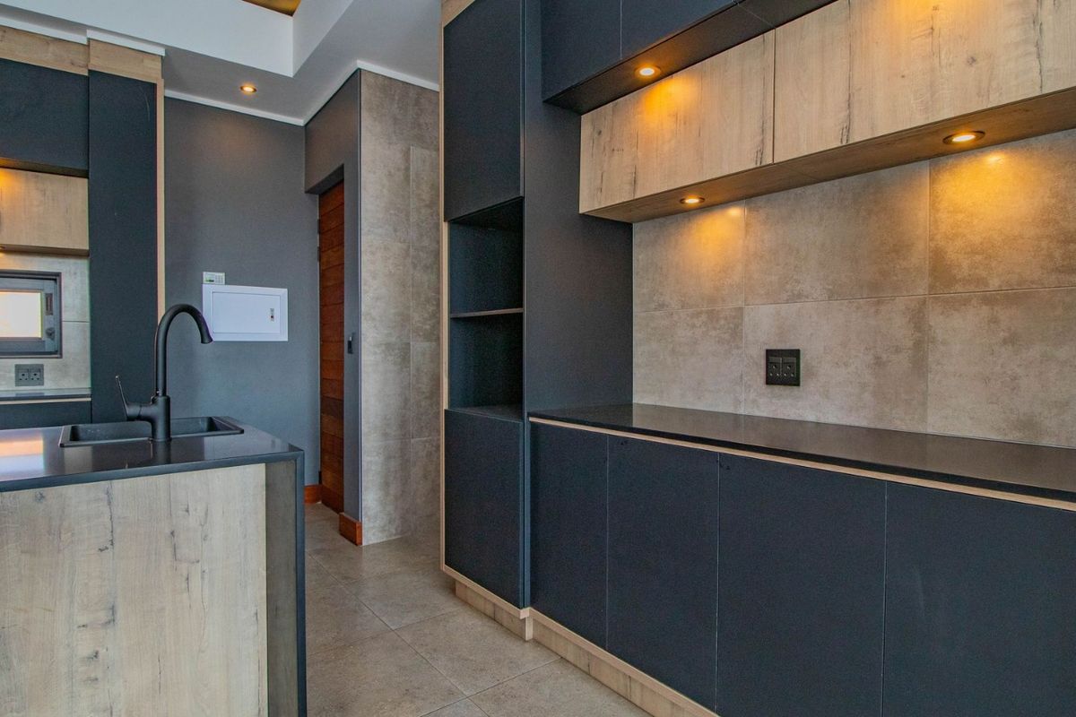 Modern kitchen featuring dark cabinetry, light wood accents, stone countertops, integrated lighting, and high-quality tiled finishes throughout.