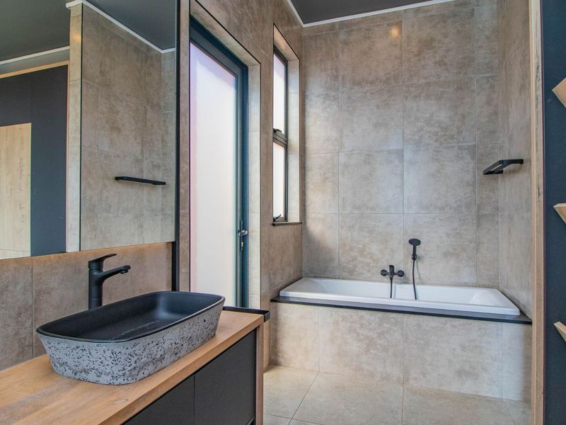 Modern bathroom featuring a sleek vessel sink, built-in bathtub with black fixtures, tiled finishes, and floating shelving in a contemporary design.
