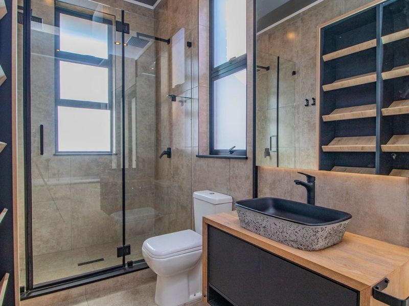 Modern bathroom featuring a walk-in shower with glass screen, vessel sink on a wooden vanity, and built-in shelving with contemporary black matte fixtures.