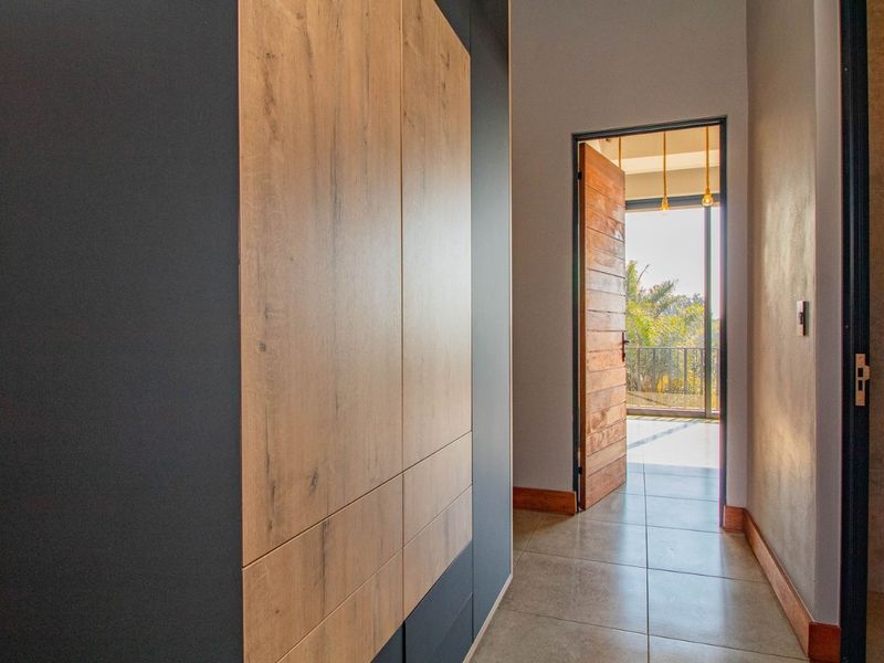 A modern hallway featuring sleek built-in cabinetry with wood-grain accents, tiled flooring, and a timber door leading to an outdoor balcony area.