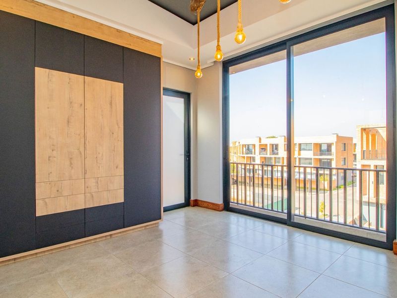 Modern bedroom featuring built-in cupboards, large sliding glass doors leading to a balcony, and contemporary tiled flooring.