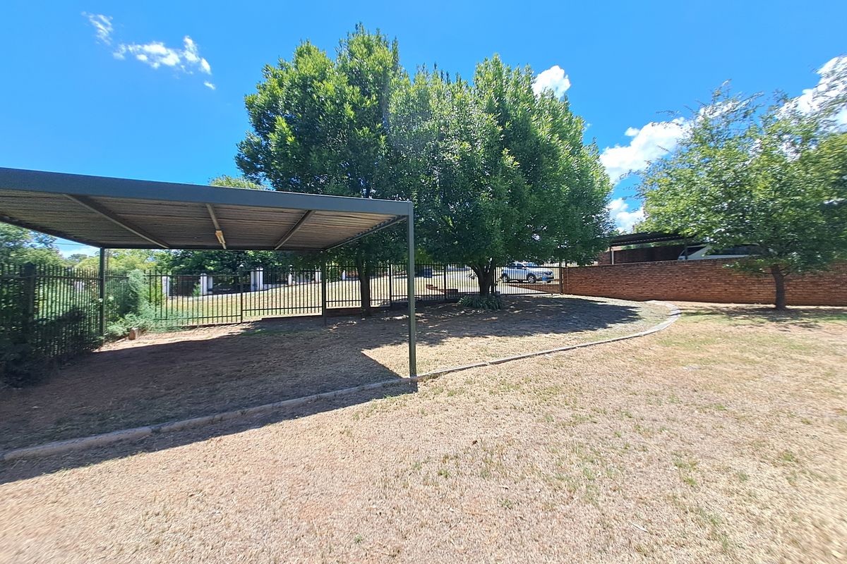 A spacious rear garden area featuring a functional metal carport, secure perimeter fencing, and established trees, providing ample outdoor space.