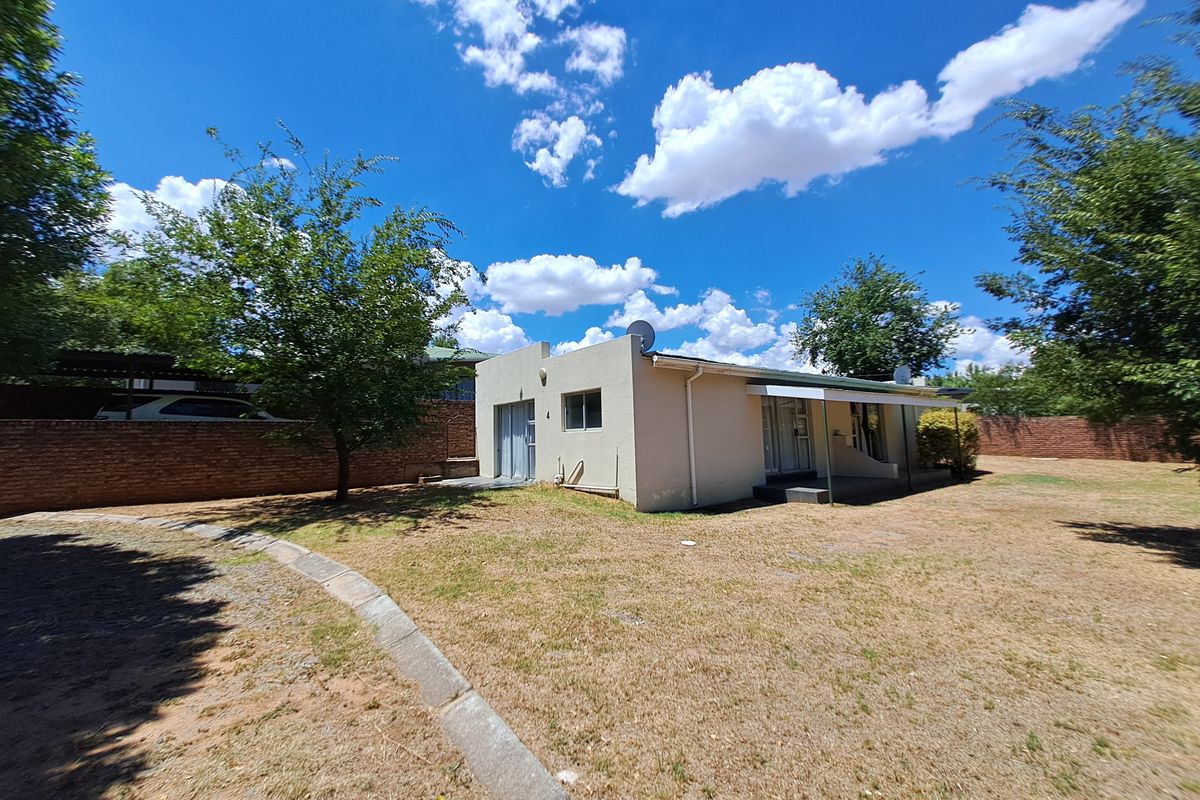 Rear view of the property featuring a spacious yard, brick boundary walls, and a covered patio area.