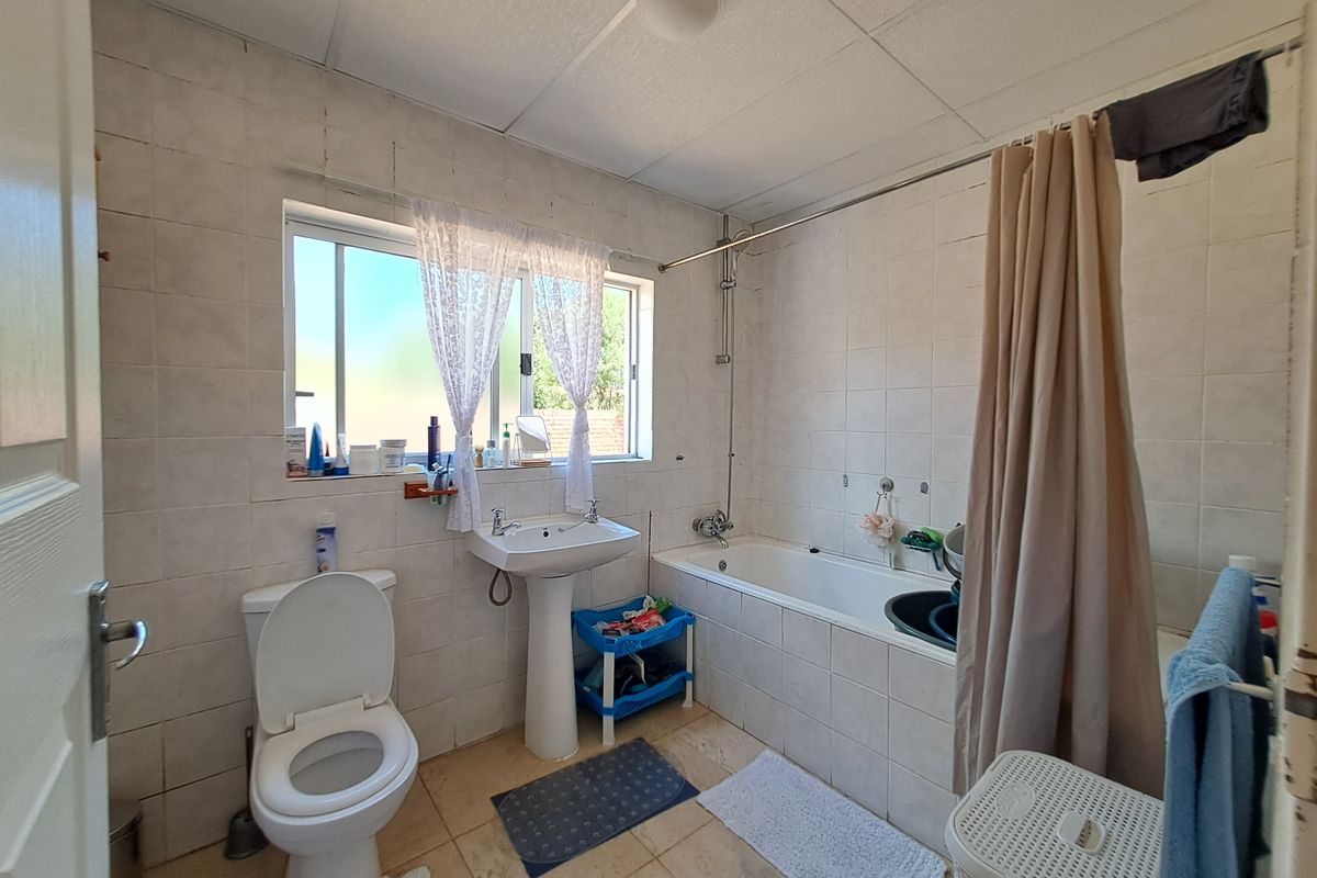 A dated bathroom featuring a pedestal basin, bathtub with shower mixer, and full-height wall tiling, requiring cosmetic updates to improve its overall condition.