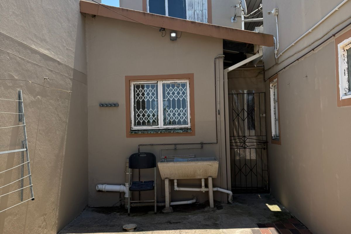 A narrow rear exterior courtyard featuring concrete paving, a utility sink, and security gates, providing access to the rear of the property.