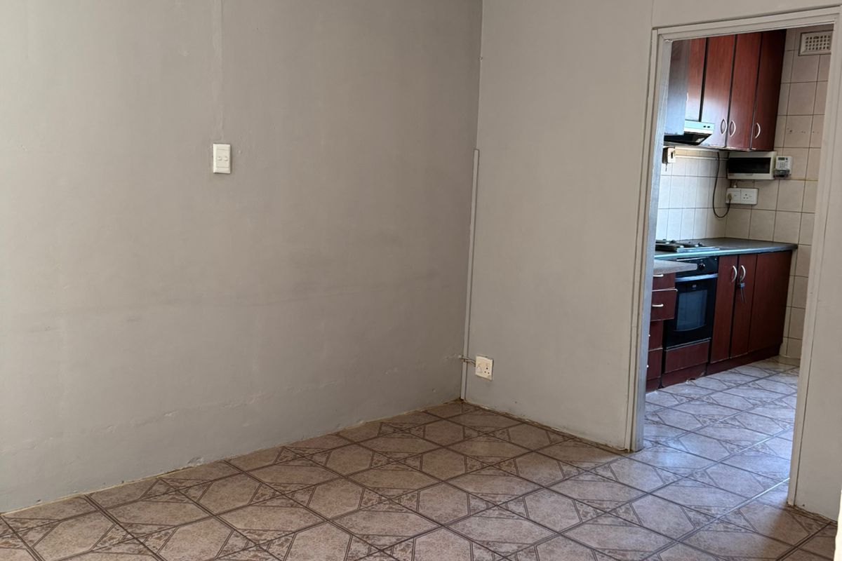 An empty living area with tiled flooring, leading through a doorway into a kitchen featuring dark wood cabinetry and built-in appliances.
