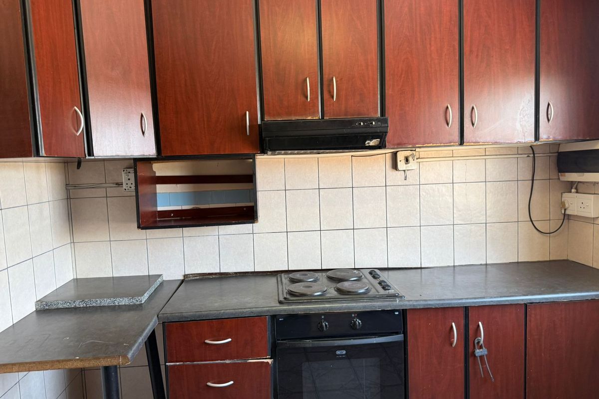 A dated kitchen featuring dark wood-look cabinetry, a built-in oven and hob, and a tiled backsplash with a functional layout.