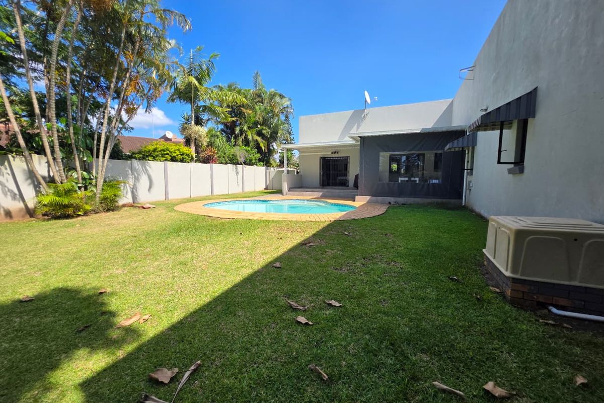 A spacious rear garden featuring a swimming pool with brick coping, a well-maintained lawn, and a covered patio area attached to the main house.