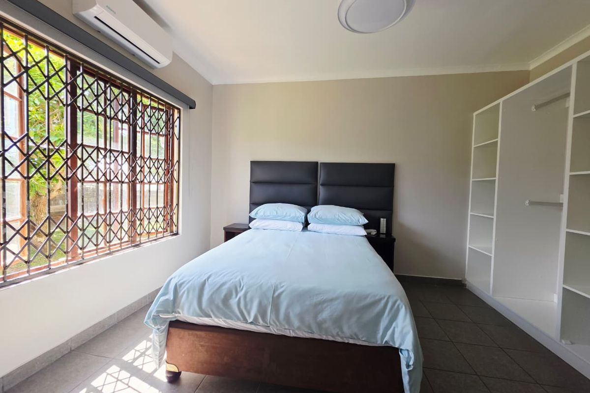 A well-lit bedroom featuring tiled flooring, a split-system air conditioner, and built-in shelving units, with security gates installed on the window.
