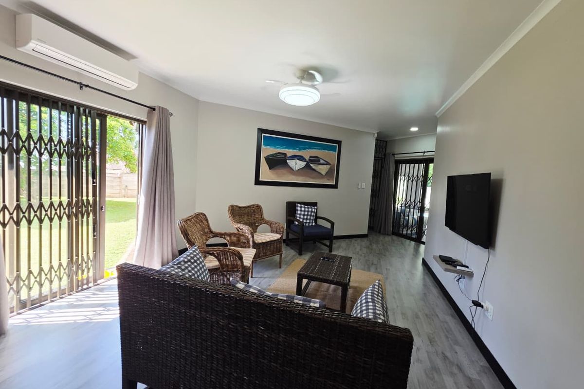 A bright living room featuring laminate flooring, a ceiling fan, and a split-system air conditioner, with direct access to the garden through a sliding door.