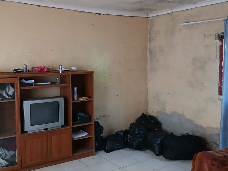 A bedroom space requiring significant renovation, featuring tiled floors and visible wall and ceiling damage throughout the room.