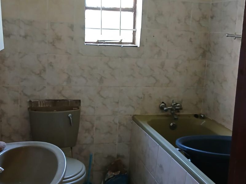 A dated bathroom featuring original sanitary ware, tiled walls, and a window with security bars, requiring modernization and cosmetic updates.