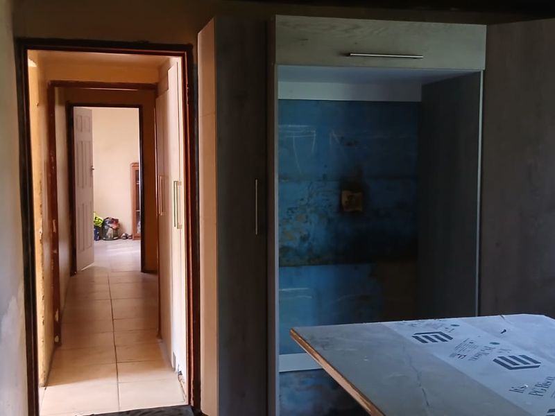 A kitchen area under renovation featuring built-in cabinetry and a sink, with unfinished walls requiring completion.