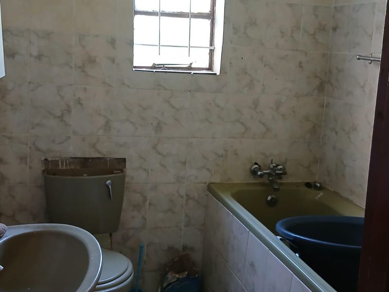 A dated bathroom featuring original fixtures, including a bathtub, toilet, and washbasin, with tiled walls and a window with security bars.