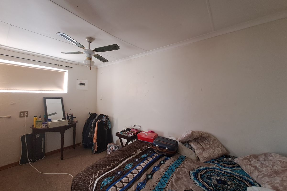 A bedroom featuring a ceiling fan, carpeted flooring, and a roller blind. The room requires cosmetic updates to improve its overall condition.