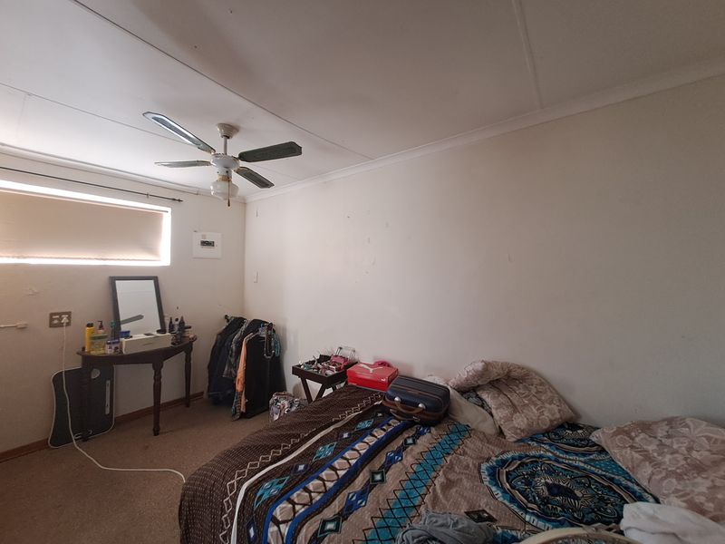 A bedroom featuring a ceiling fan, carpeted flooring, and a roller blind. The room requires cosmetic updates to improve its overall condition.