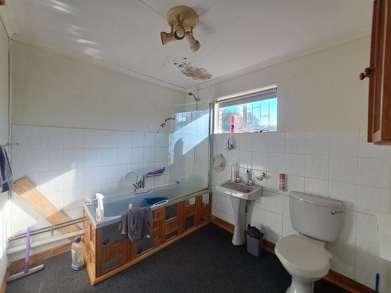 A dated bathroom featuring a bathtub with a glass screen, pedestal sink, and toilet, requiring significant cosmetic updates and repairs to the ceiling and walls.