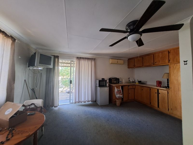 Open-plan living area featuring a kitchenette with wooden cabinetry, ceiling fan, wall-mounted air conditioning, and direct access to an outdoor patio area.