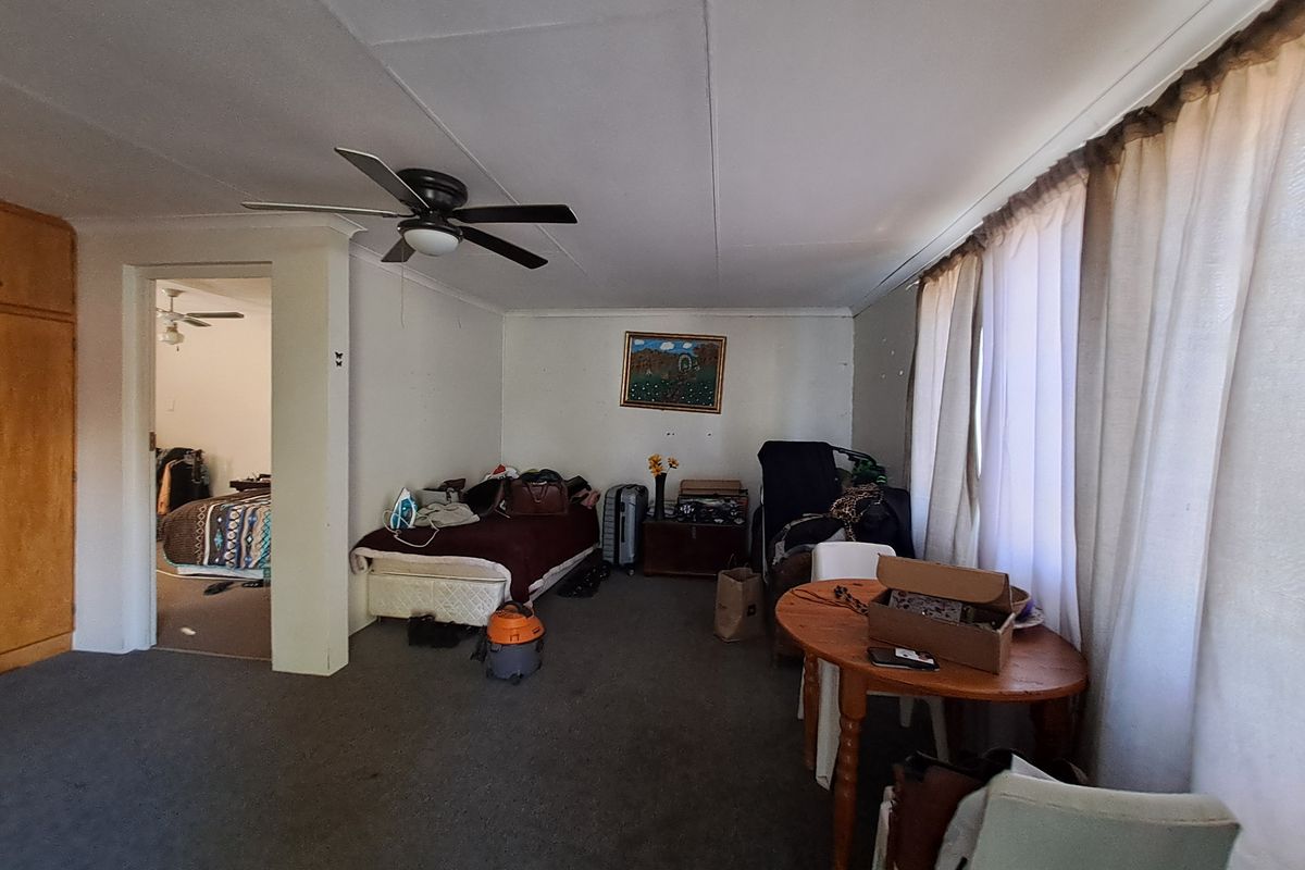A living room area featuring a ceiling fan and built-in storage, with carpet flooring and access to an adjacent bedroom.