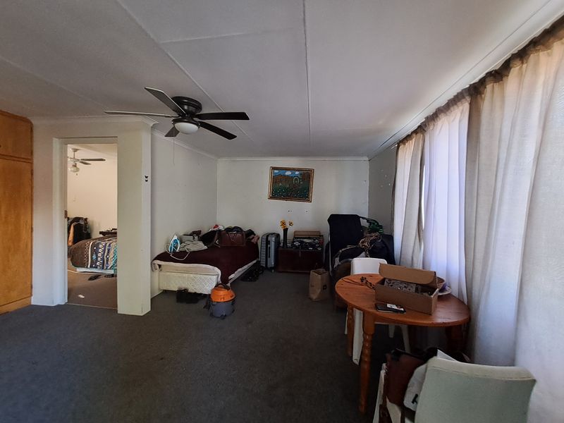 A living room area featuring a ceiling fan and built-in storage, with carpet flooring and access to an adjacent bedroom.