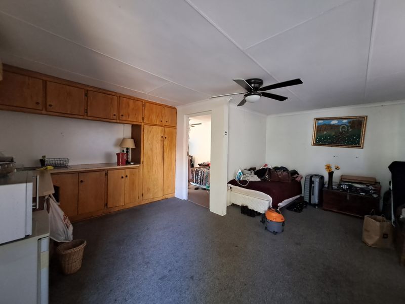 Open plan living area featuring built-in wooden cabinetry, a ceiling fan, and carpeted flooring, providing a functional space with potential for modernization.