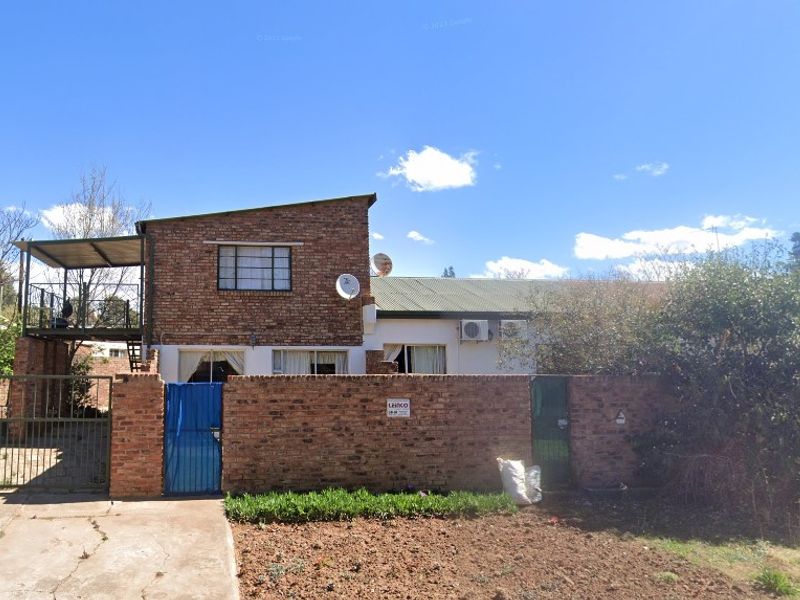 Front view of a brick house featuring a boundary wall, gated entrance, and an elevated balcony area.