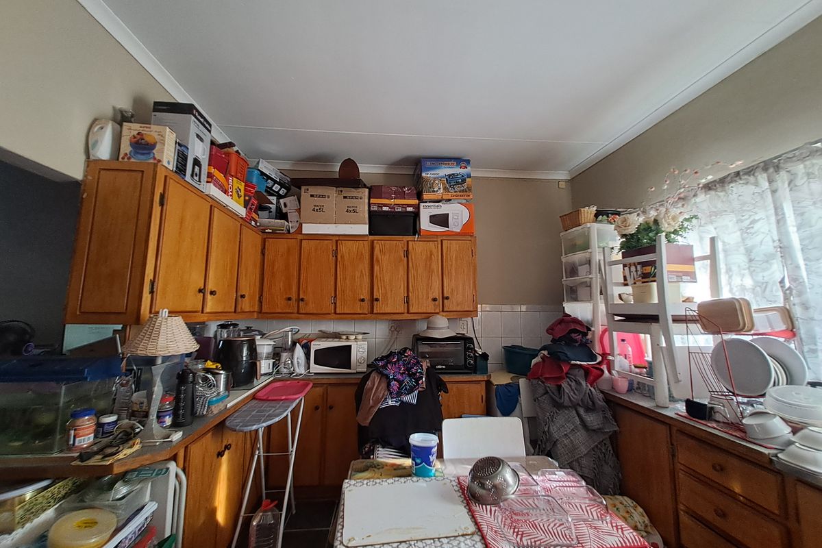A kitchen featuring wooden cabinetry, tiled backsplash, and laminate countertops, currently cluttered with various household items.