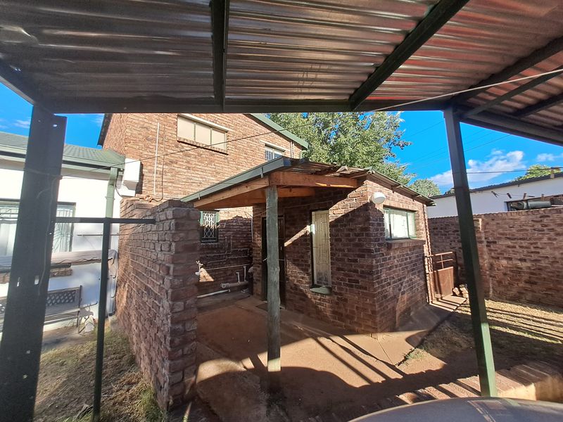 Rear exterior view showing a brick structure with a corrugated metal carport and exposed timber framing.