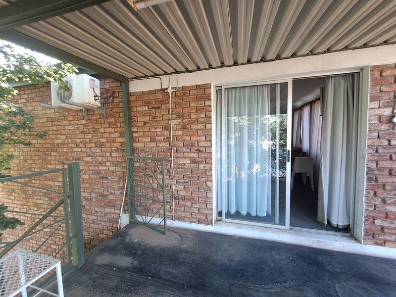 A covered patio area featuring exposed brick walls, a sliding glass door entrance, and a corrugated metal roof structure.