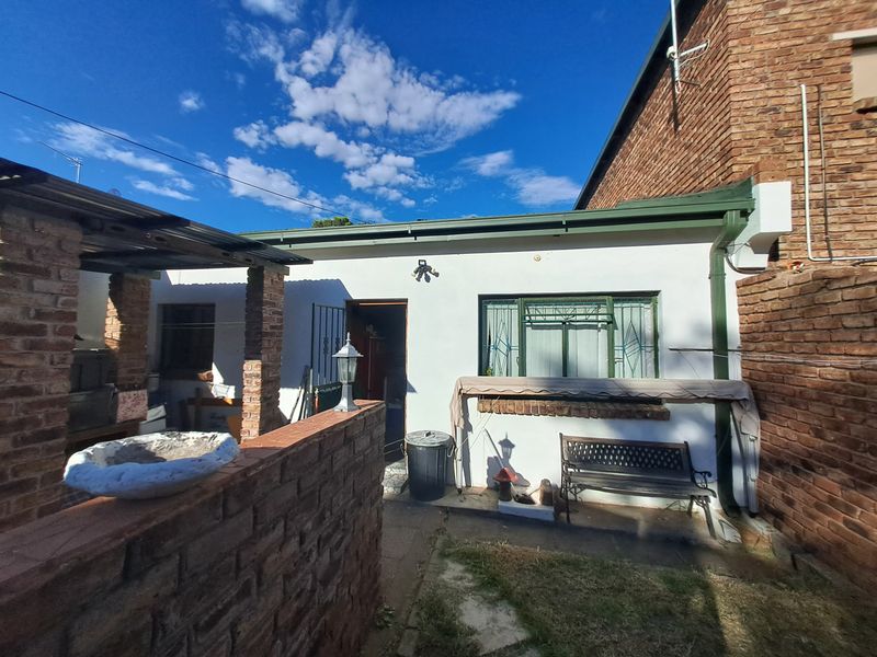 Rear exterior view of the property featuring a covered patio area, brick construction, and security features on windows and doors.