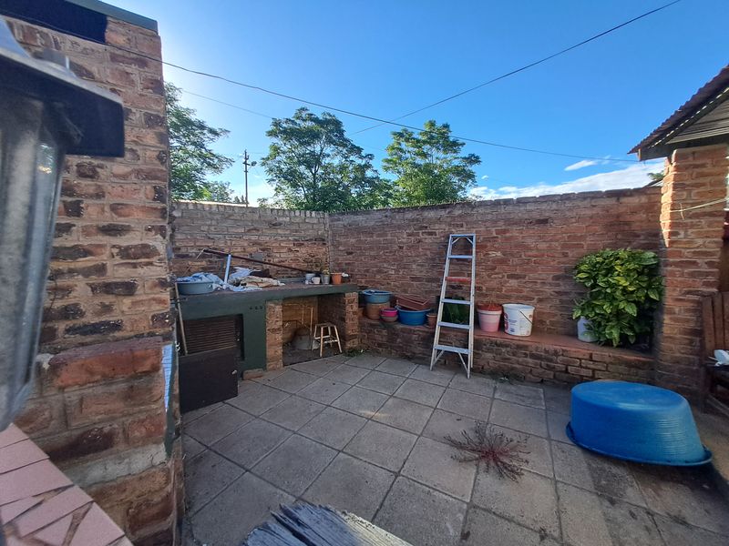Outdoor patio area featuring a built-in brick braai and paved flooring, enclosed by a brick perimeter wall.