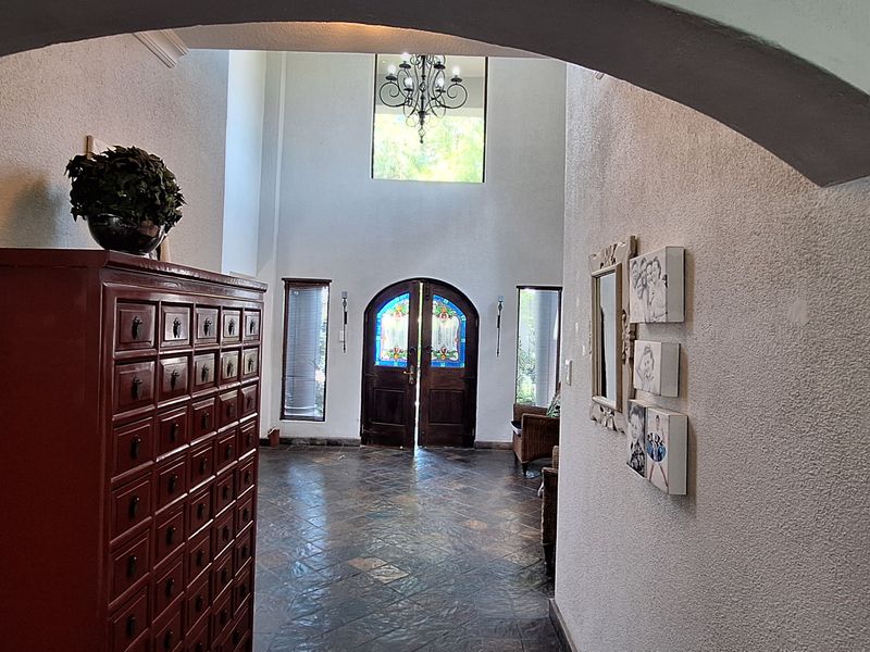 Spacious double-volume entrance hall featuring stone tile flooring, an arched entryway, and elegant double doors with stained glass detailing.