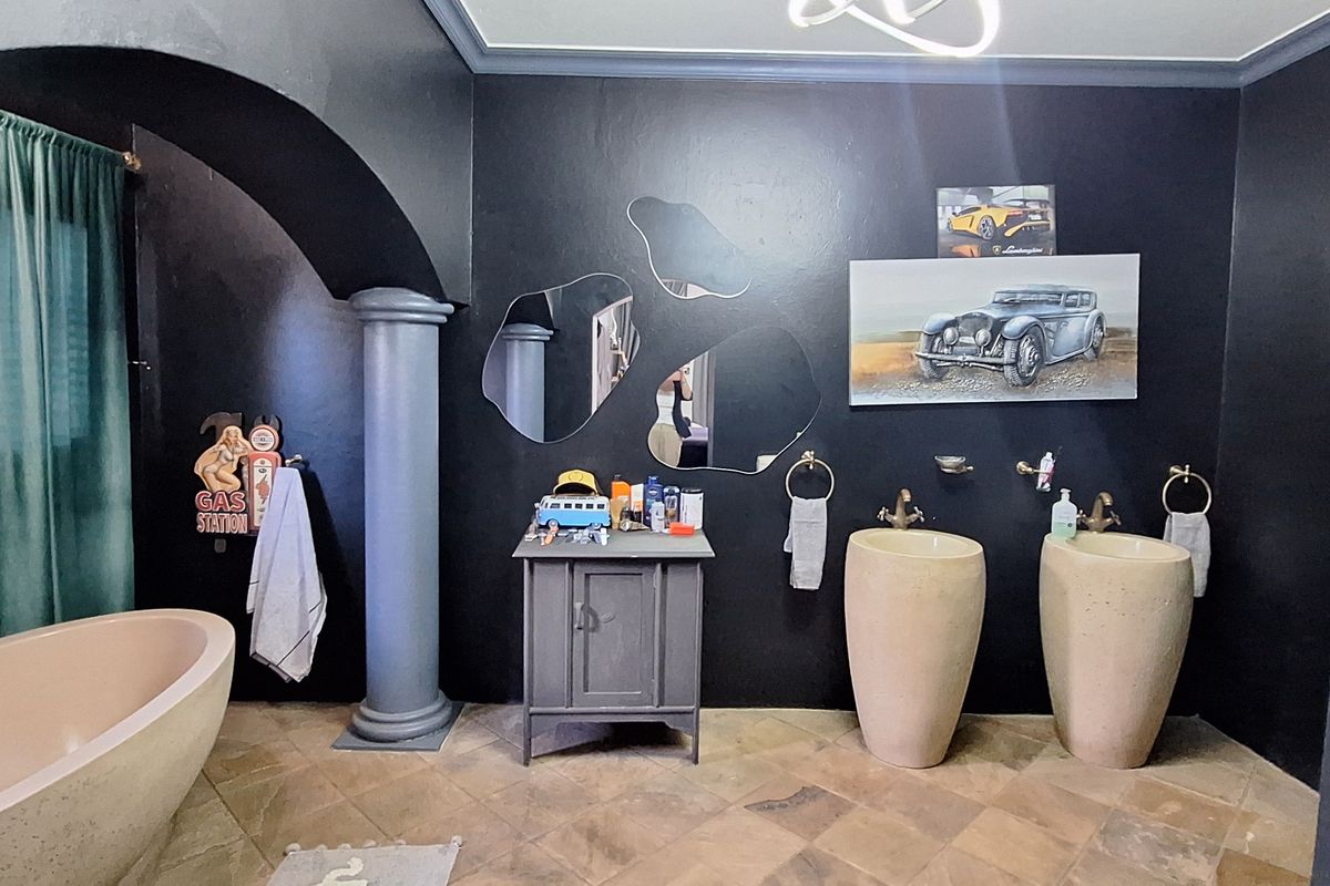 A uniquely styled bathroom featuring a freestanding bathtub, dual pedestal basins, an architectural archway, and a decorative column against dark-painted walls.