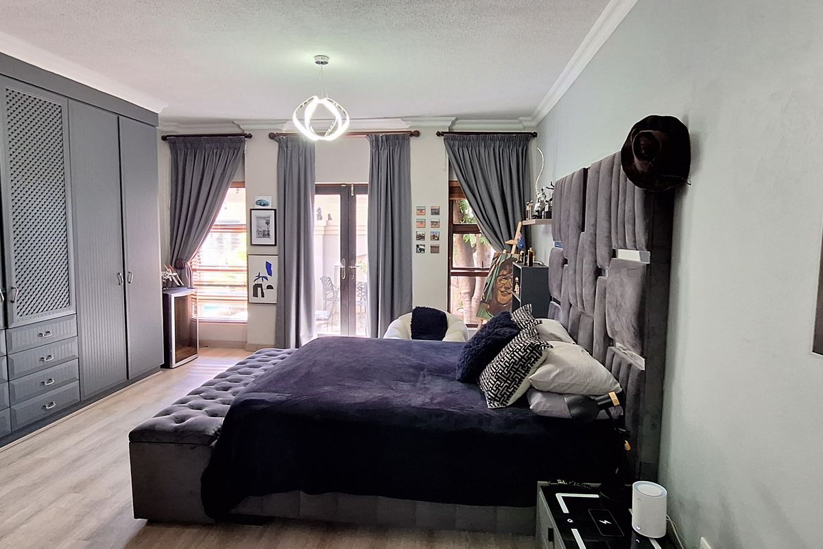 Spacious bedroom featuring extensive built-in cabinetry, light-toned laminate flooring, and direct access to an outdoor area through glass french doors.