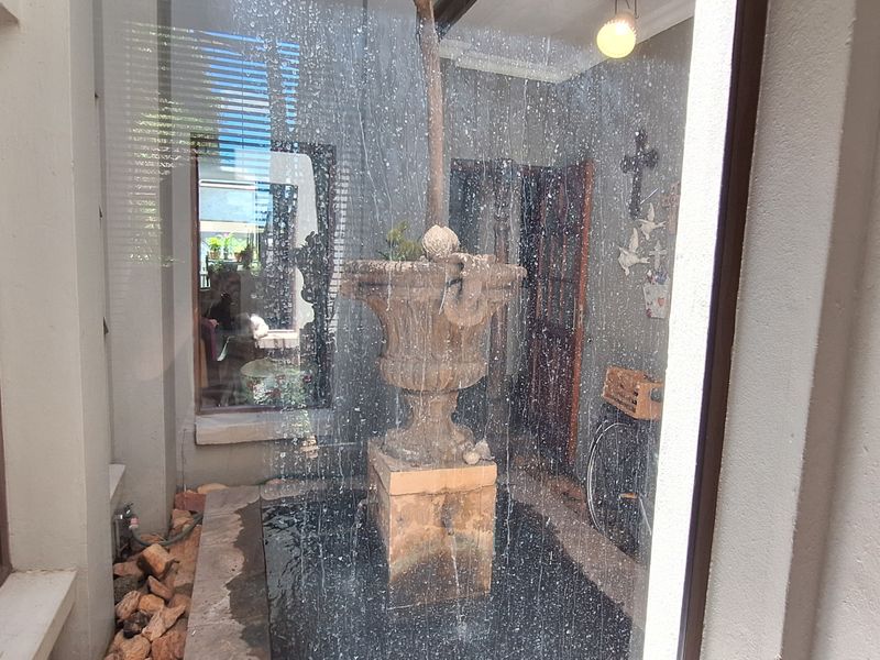 A small courtyard or patio area featuring a central stone water fountain, viewed through a glass partition.