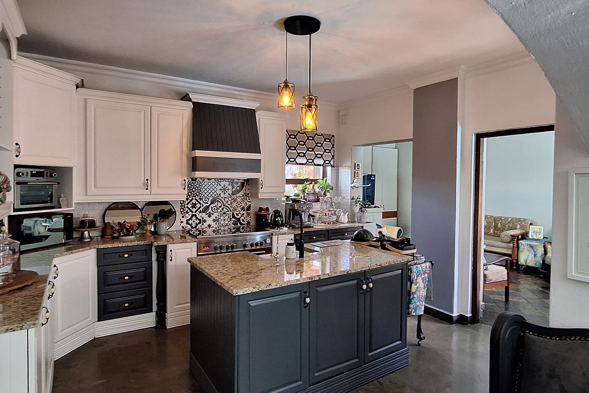 A well-appointed kitchen featuring a central island with granite countertops, shaker-style cabinetry, a built-in oven, and a decorative patterned tile backsplash.