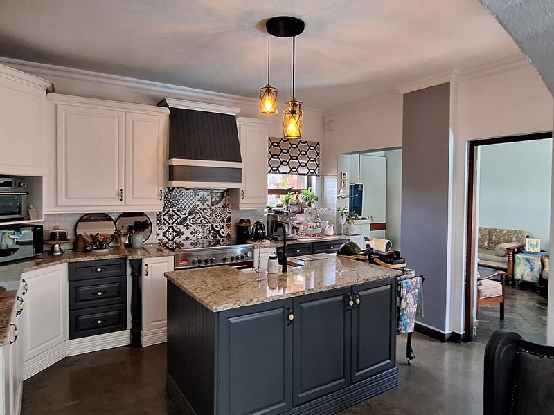A well-appointed kitchen featuring a central island with granite countertops, shaker-style cabinetry, a built-in oven, and a decorative patterned tile backsplash.
