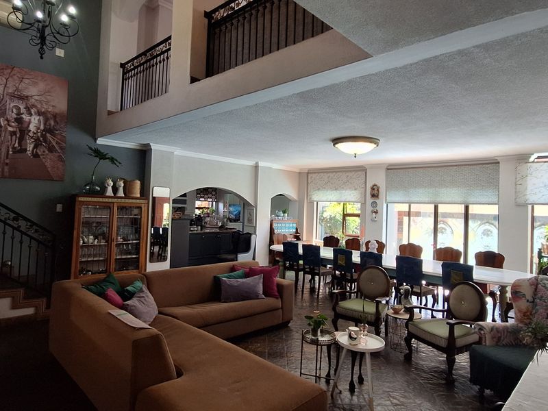 Spacious open-plan living and dining area featuring a double-volume ceiling, wrought iron staircase, and mezzanine level overlooking the main floor.