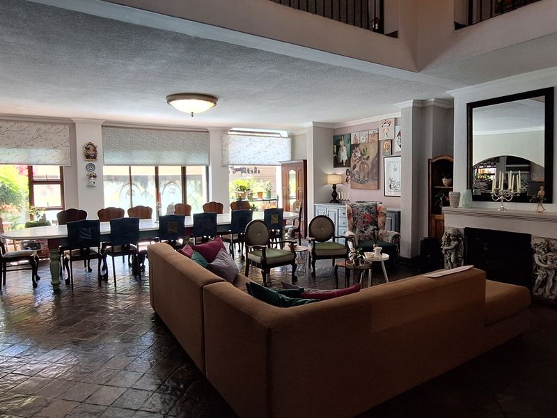 Spacious open-plan living and dining area featuring stone tile flooring, a fireplace, and a double-volume ceiling with an elegant wrought iron staircase.