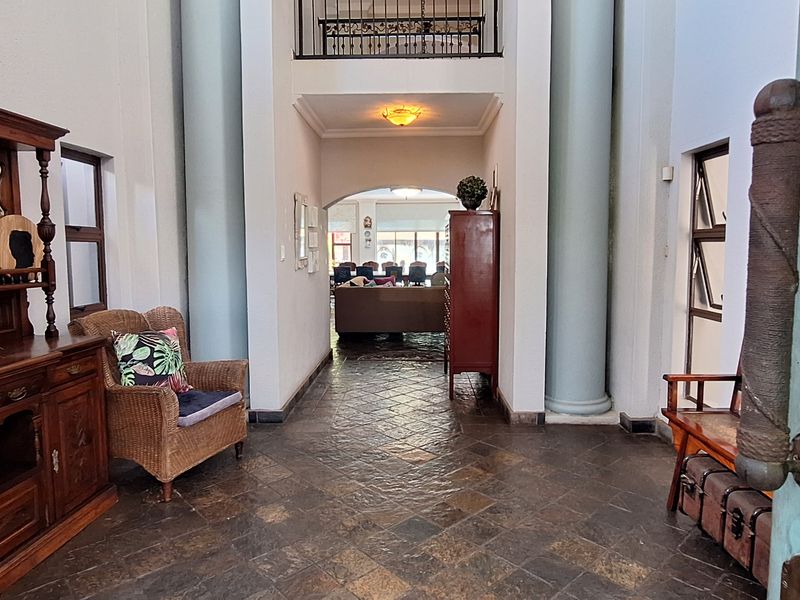 Spacious double-volume entrance hall featuring tiled flooring, decorative columns, and a mezzanine landing with a wrought iron balustrade.