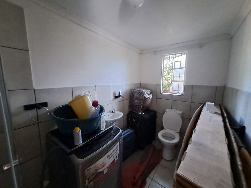 A functional laundry and utility room featuring tiled walls, a wall-mounted basin, and a toilet, with a window providing natural light.